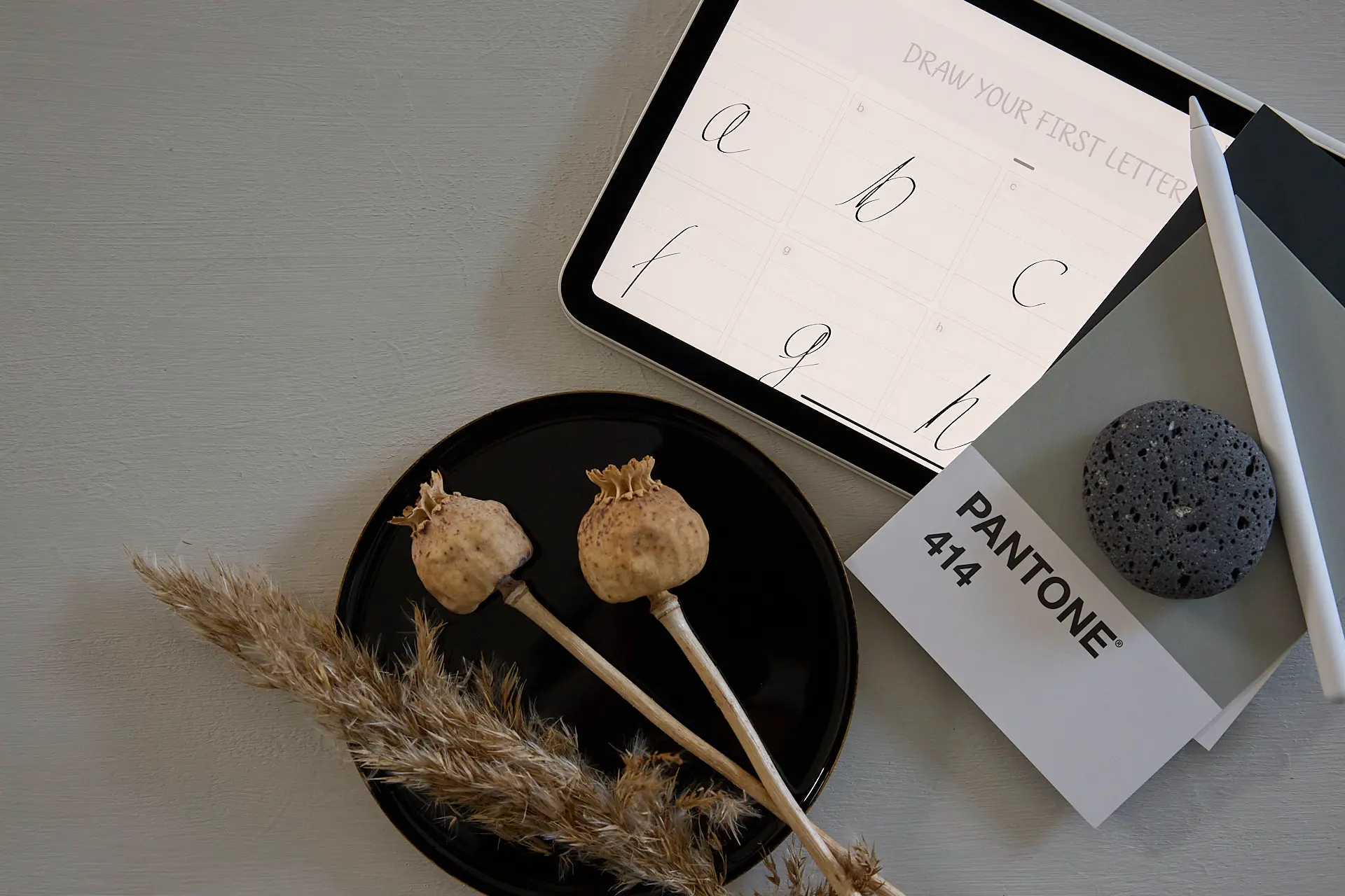 2024-08-18 Nadine Cardenäo 154 Tablet mit Schreibübungen und Dekorationselementen wie einer schwarzen Schale und Trockenblumen.