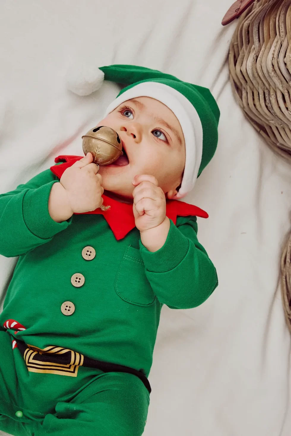 Ein Baby in einem grünen Weihnachtsmannkostüm mit einer Glocke in der Hand und einem weißen Hut auf dem Kopf.