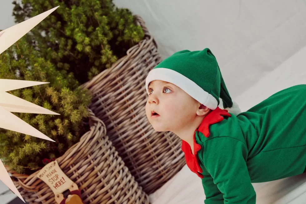 Ein Baby in einem grünen Elfenkostüm mit rotem Kragen schaut nach oben.
